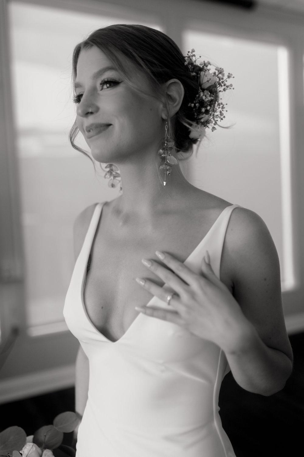 Black and white portrait of smiling bride in white gown with floral hair accessories and drop earrings.