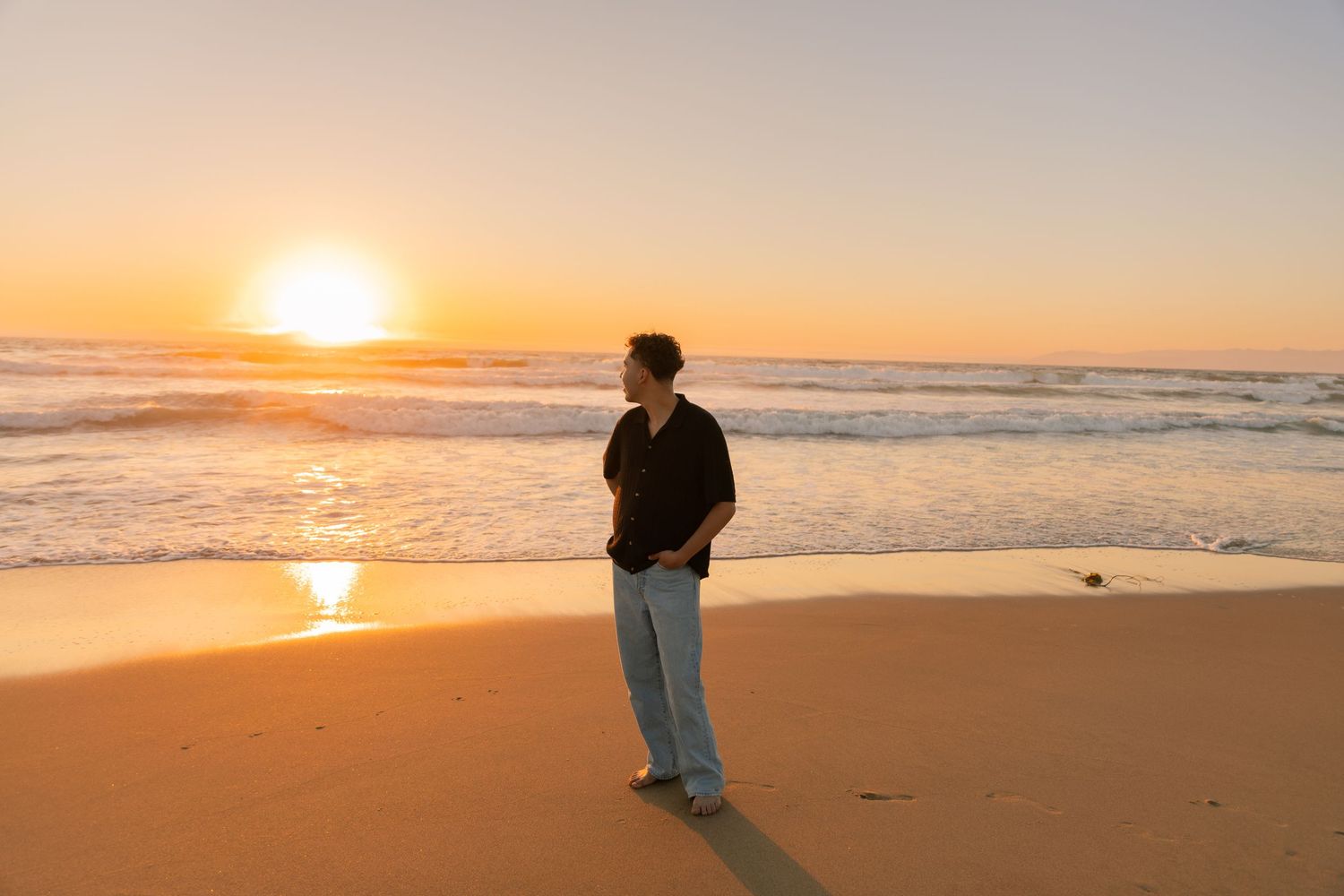 Woman in white shirt sits thoughtfully in tall golden grass during sunset.