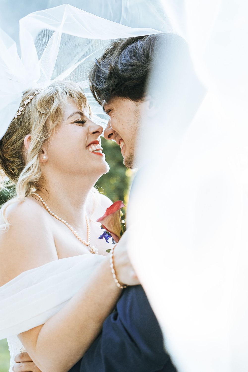 Intimate wedding moment captured through flowing white veil in outdoor setting.