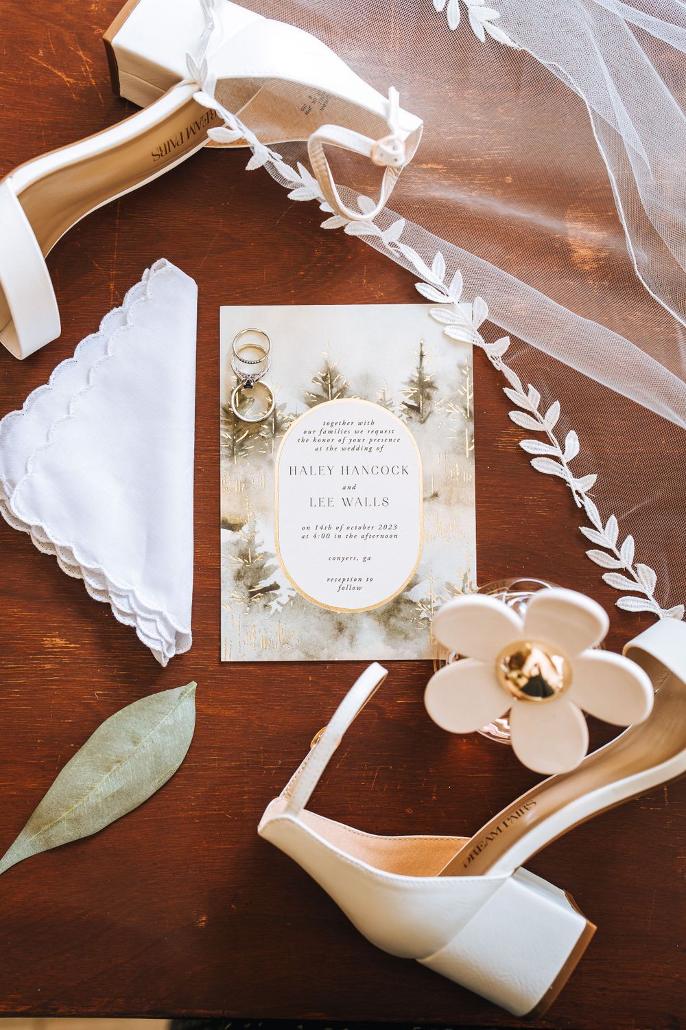 Wedding invitation with floral design alongside white shoes and veil on wooden surface.