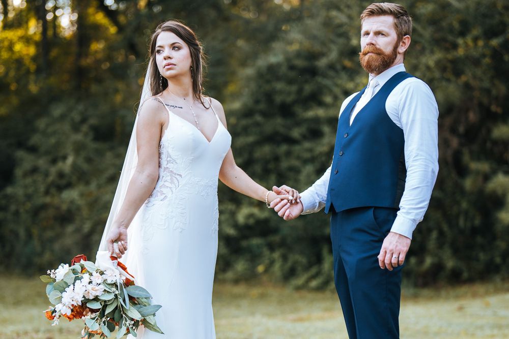Newlywed couple holding hands outdoors with autumn foliage in background.