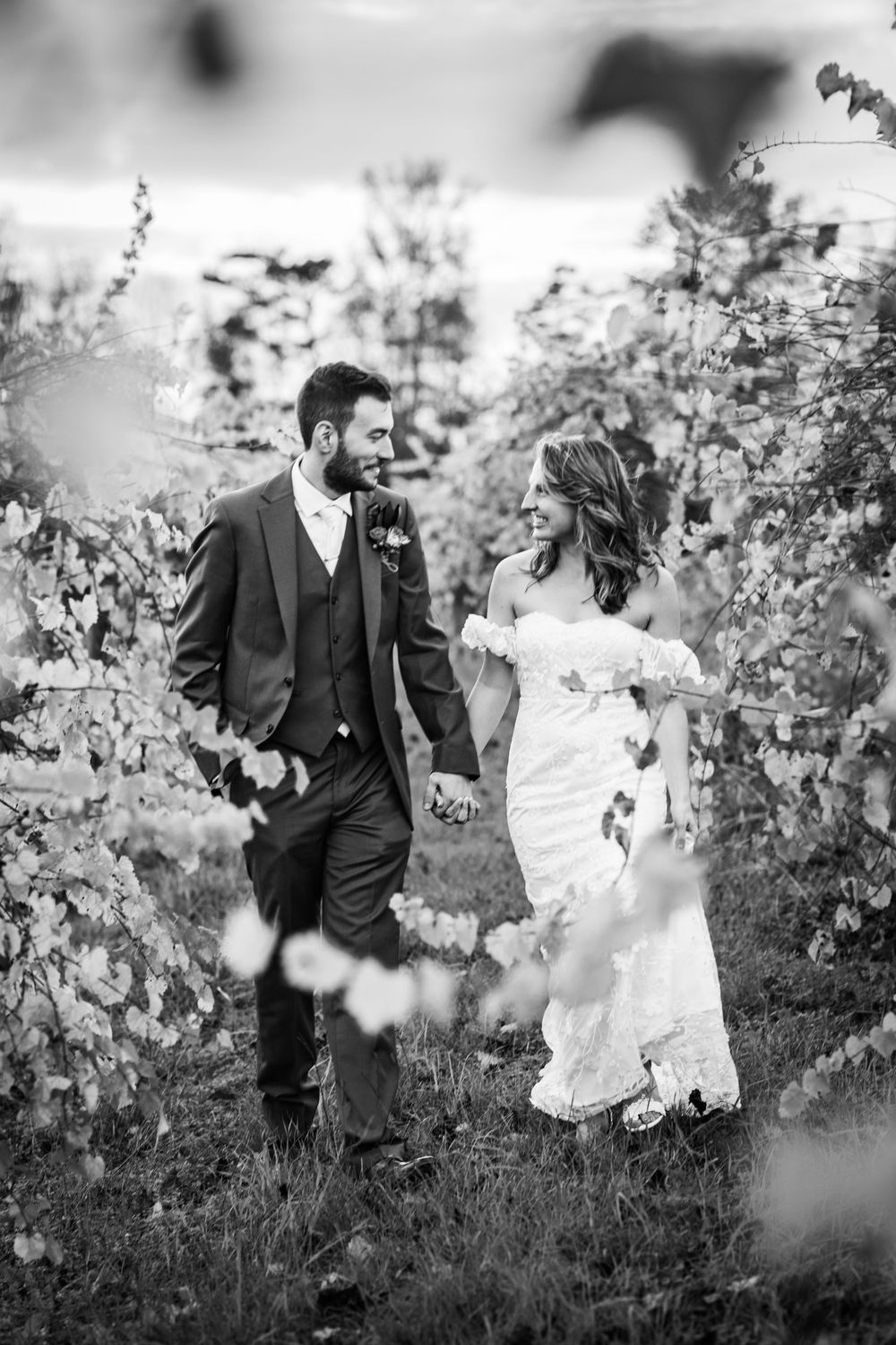 A couple in wedding attire walk together through a blooming garden in black and white.