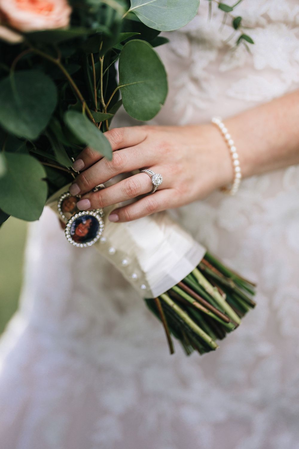 Close-up of bride's hand holding bouquet with pearl bracelet and engagement ring.