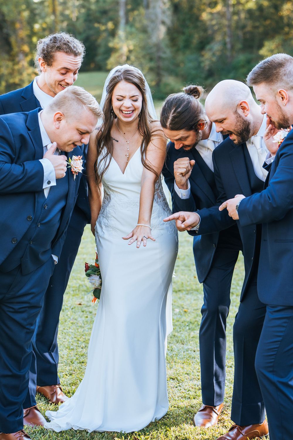 Wedding party in navy suits laughing together on grassy lawn.