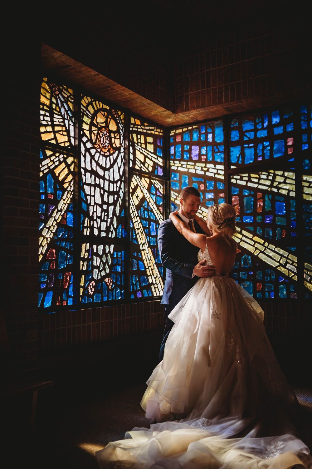 A couple dances in a romantic moment beneath colorful stained glass windows in a church setting.