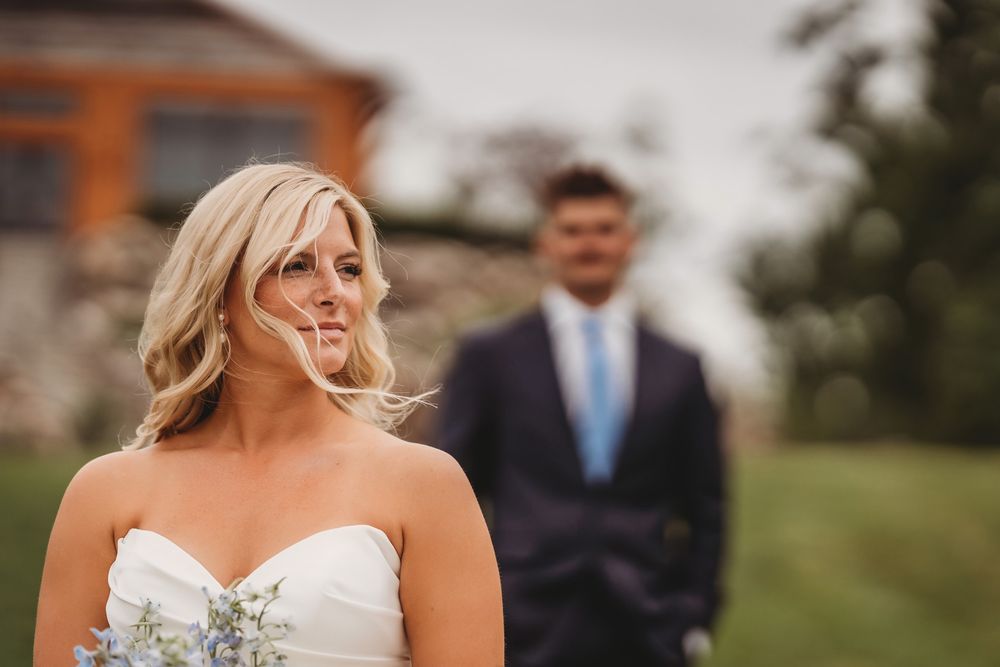 A bride in a white strapless wedding dress poses outdoors on a sunny day with a scenic background.