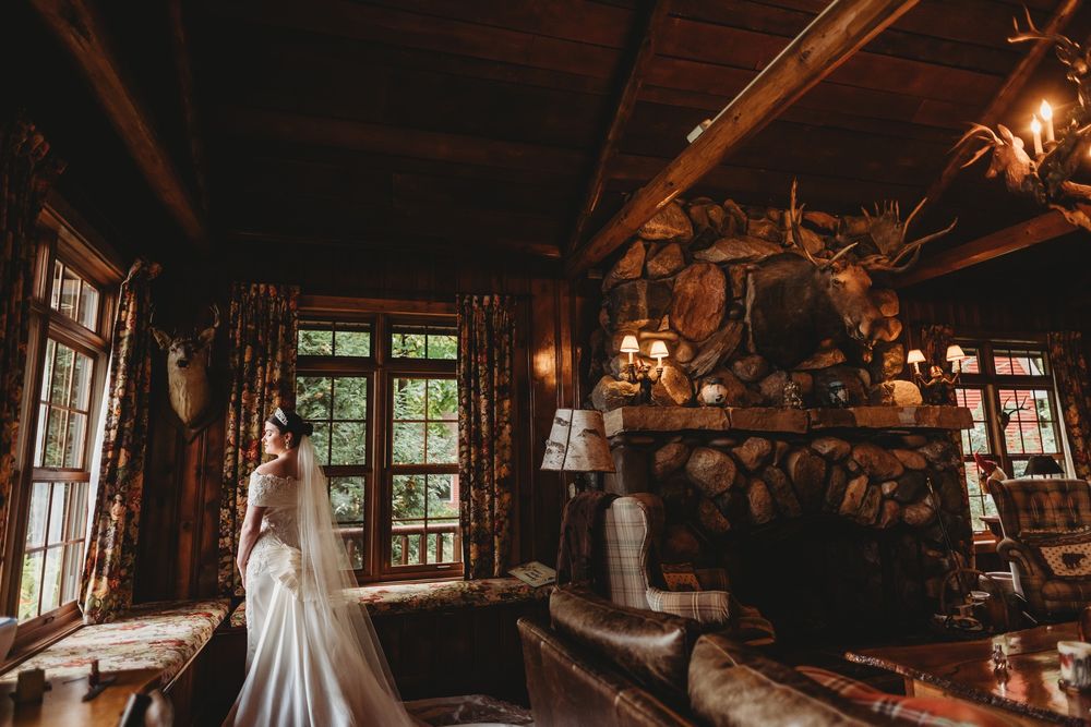 A rustic log cabin interior with a stone fireplace and warm lighting creates a cozy atmosphere for a wedding photo.
