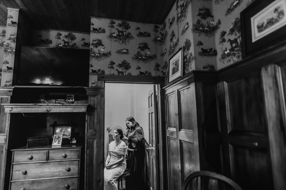 A vintage black and white photograph shows a residential interior with wallpapered walls and antique furnishings.