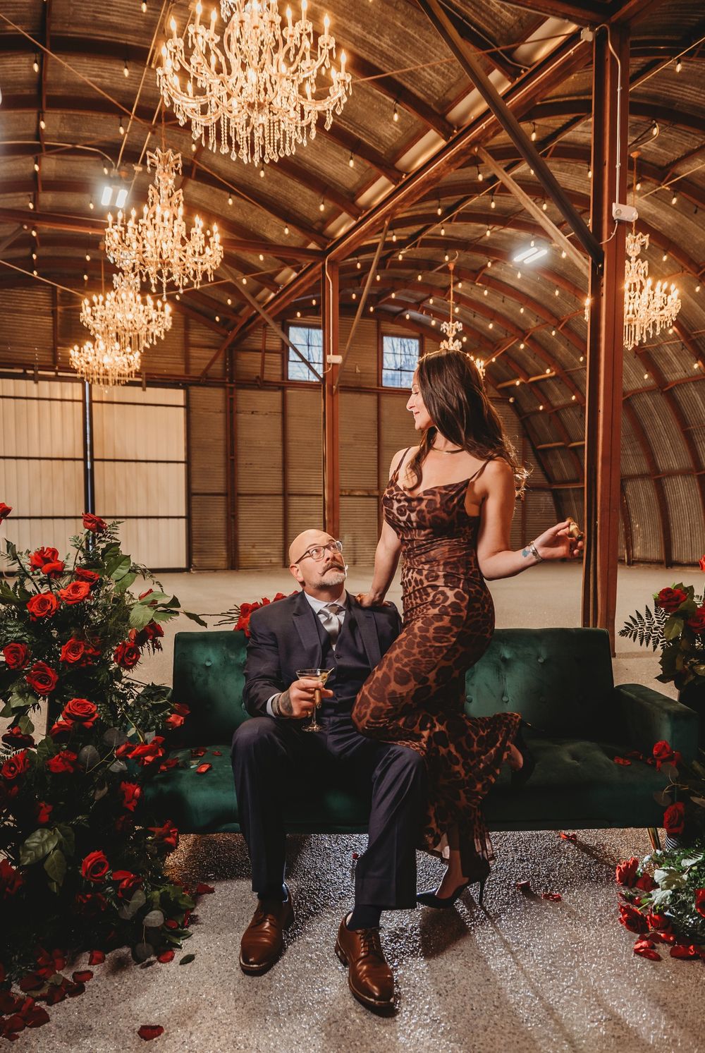 A romantic proposal scene unfolds in a rustic barn venue with crystal chandeliers and red roses as decorative elements.