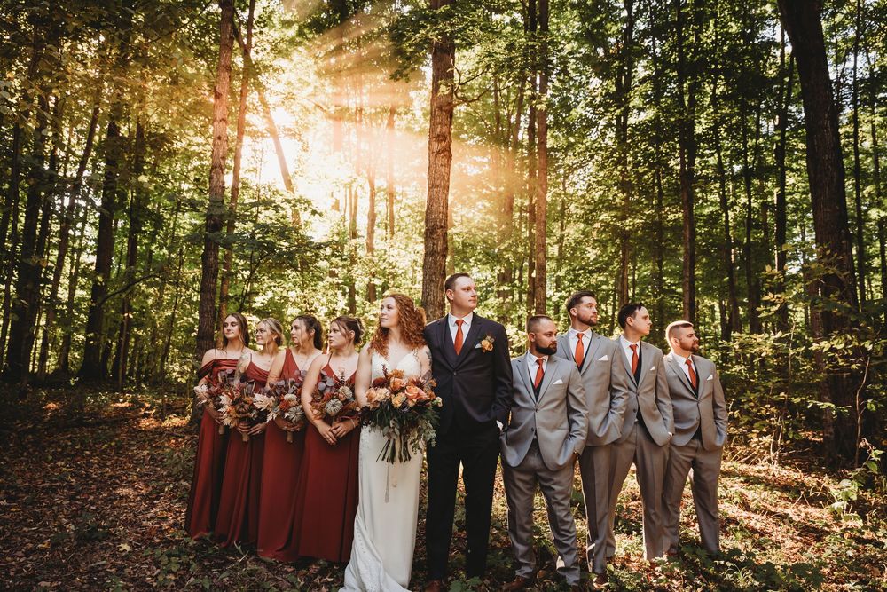 Wedding party poses together in a sunlit wooded area during autumn.