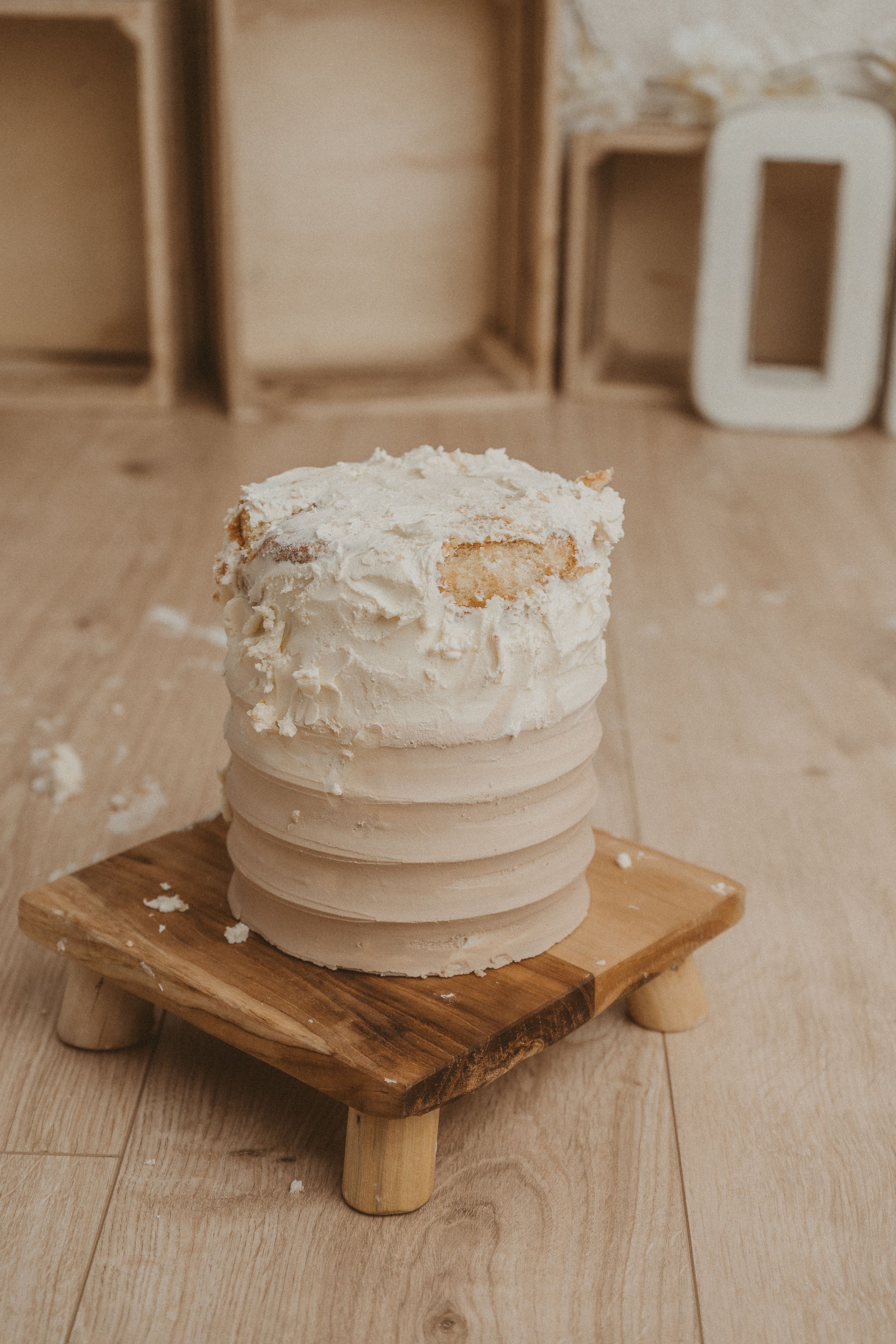 A rustic white wedding cake with textured frosting sits on a wooden pedestal against a neutral background.