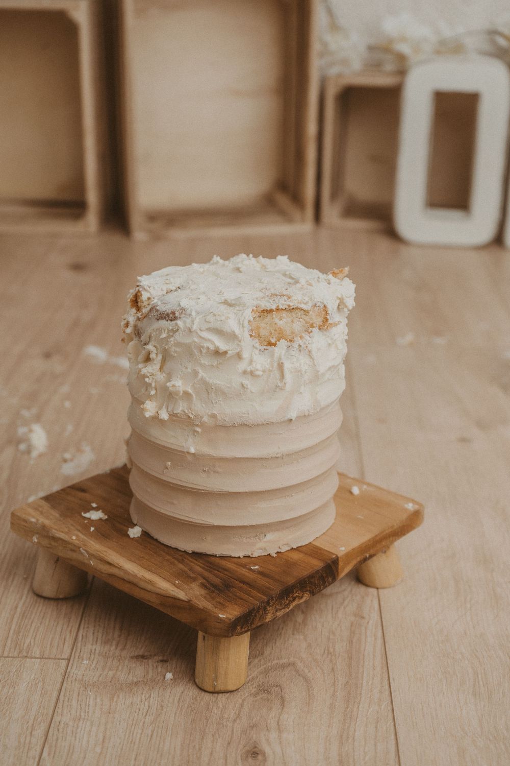 A rustic white wedding cake with textured frosting sits on a wooden pedestal against a neutral background.
