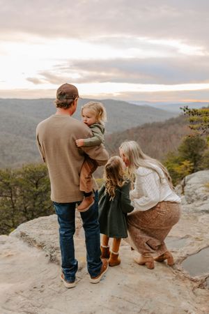 A family shares a tender moment together on a mountain overlook during sunset.
