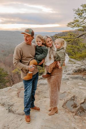A family of four poses together on a rocky mountain overlook at sunset.
