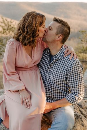 Romantic couple embracing on mountain overlook in coordinated pink and blue outfits.