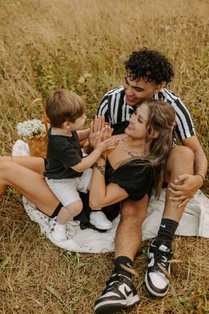 A young family shares a playful moment on a blanket in a sunny field.