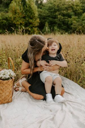 A tender family moment captured on a picnic blanket in tall grass.