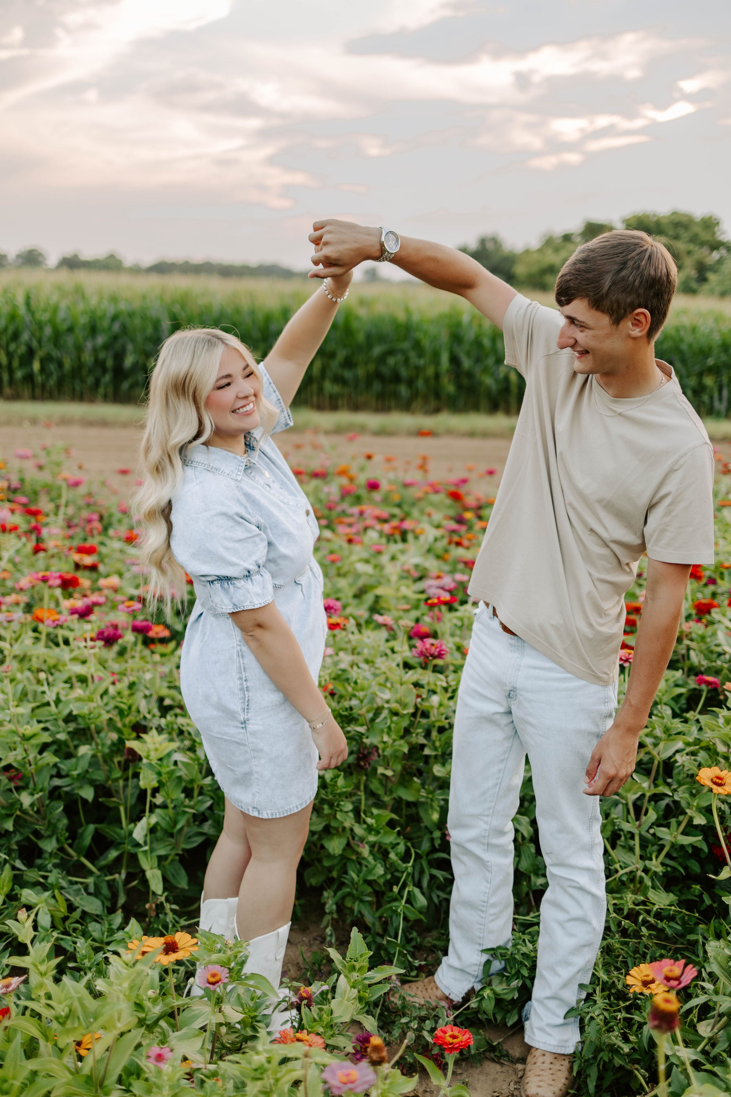 A couple poses playfully in a blooming red flower field at sunset.