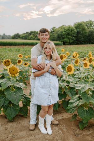 A romantic couple embraces in a vibrant sunflower field during sunset.