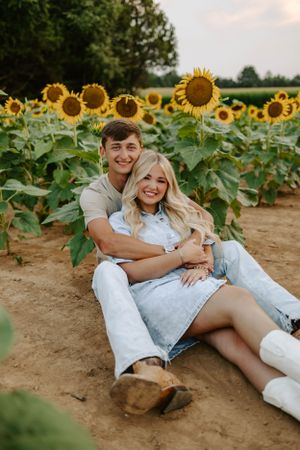 Couple sitting together surrounded by blooming sunflowers in a field.