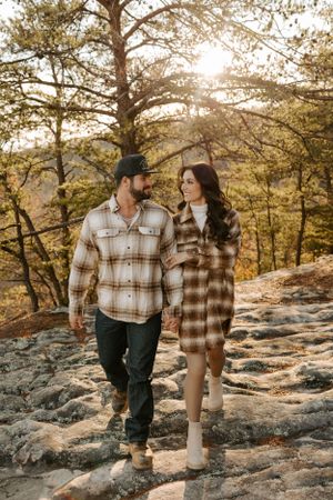 A couple in plaid flannel shirts walking together on rocky terrain during golden hour in autumn.
