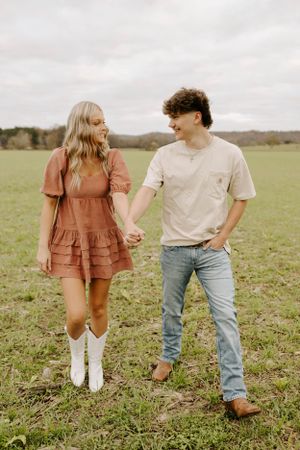 A couple in casual attire holding hands while walking through a grassy field.