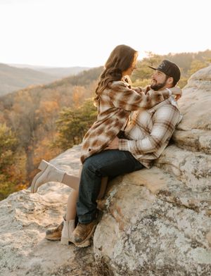 A romantic autumn moment shared on rocky cliffs overlooking a mountain landscape at sunset.