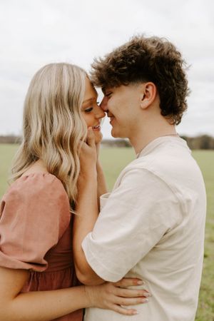 A romantic couple in a pink dress and white shirt share an intimate moment in a grassy field.