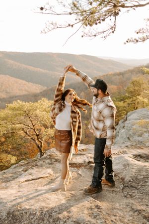 A playful dance moment on a rocky mountain overlook during sunset.