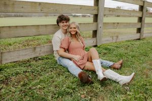 A couple relaxes together by a wooden fence in a rustic outdoor setting.