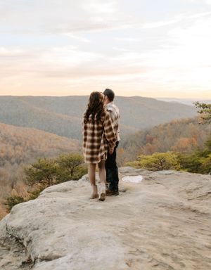 A couple admiring the sunset view from a mountain overlook in matching plaid outfits.