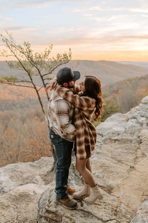 A romantic moment shared on rocky terrain with fall foliage and mountains in the background.
