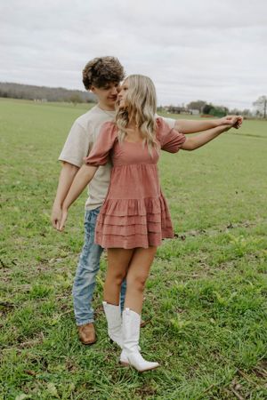 A couple in casual attire share a dance-like pose in a grassy field.