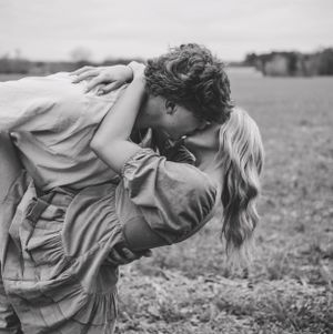 A romantic black and white photo of a couple embracing in a field.