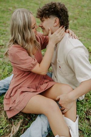 An intimate moment between a couple sitting in grass, she in pink dress and he in white shirt.