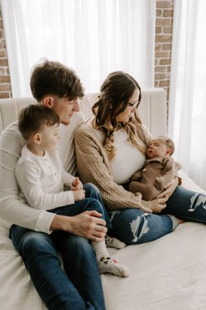A family of four cuddles together on a white couch in cozy sweaters and jeans.