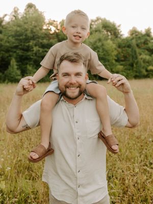 Young child sits on shoulders in a playful outdoor portrait at sunset.