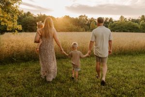 Family walks hand in hand through a golden field at sunset.
