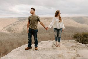 Couple holding hands while standing on scenic mountain overlook.