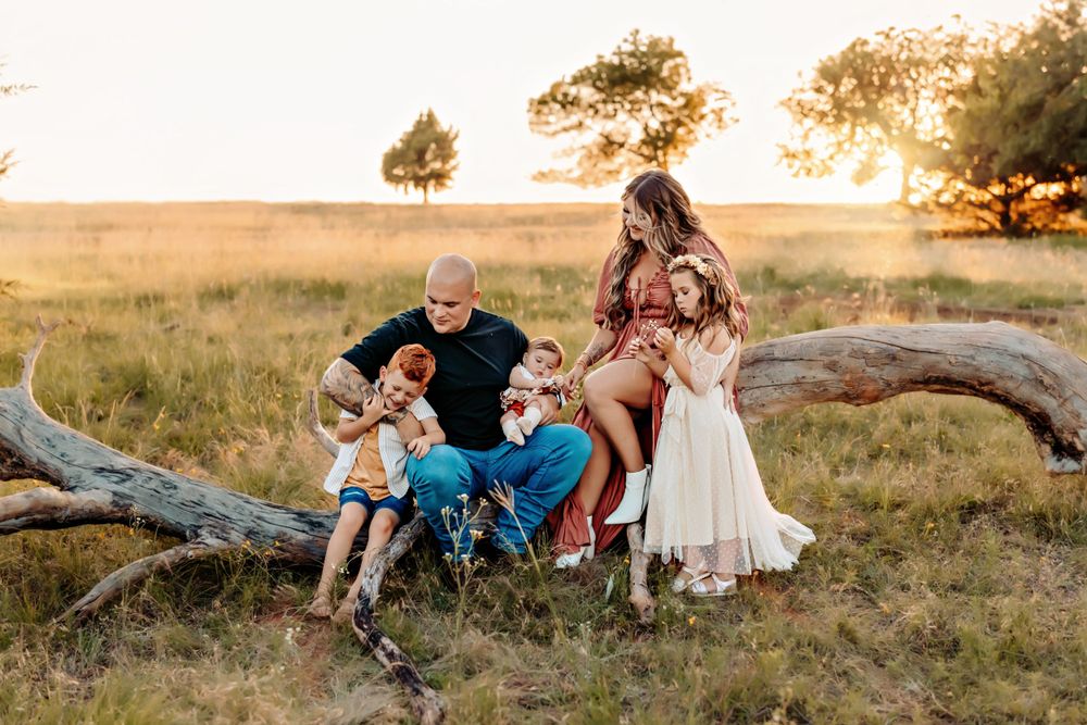 Family lounging on fallen tree in golden field during sunset.