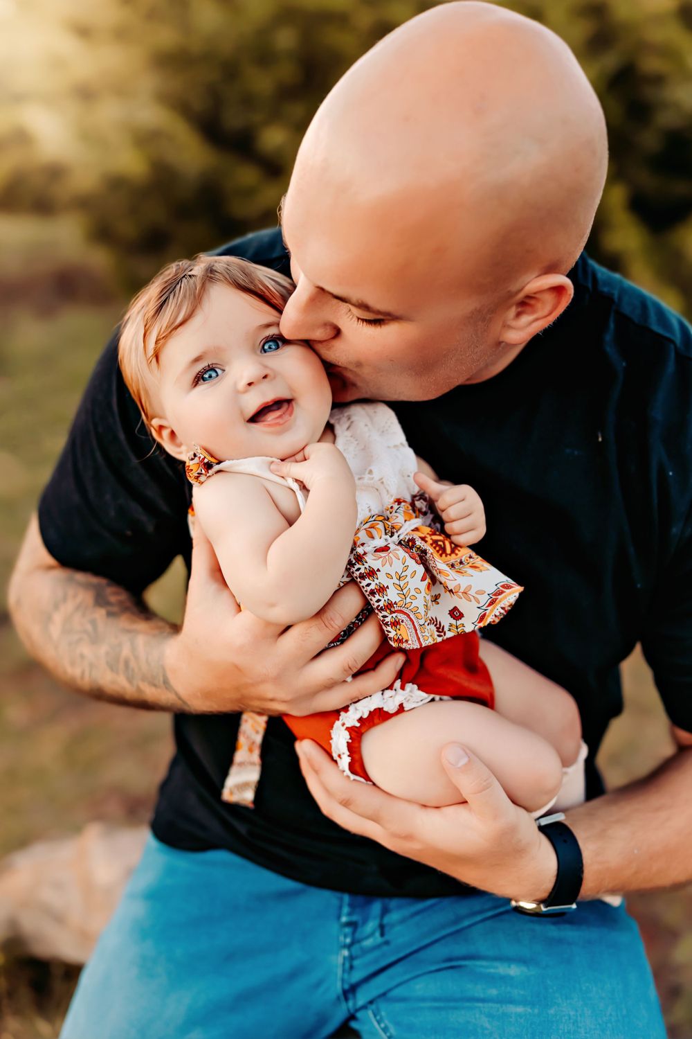 Person in black t-shirt tenderly kissing baby in floral dress.