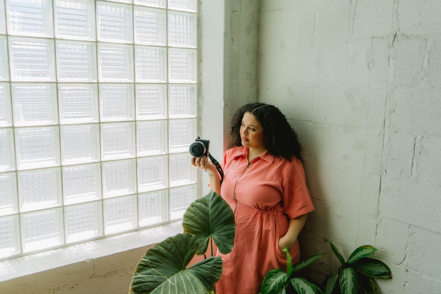 Interior scene with coral colored outfit and tropical plants near window.