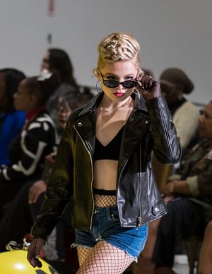 Edgy streetwear look with leather jacket, crop top, and fishnet stockings in urban setting.