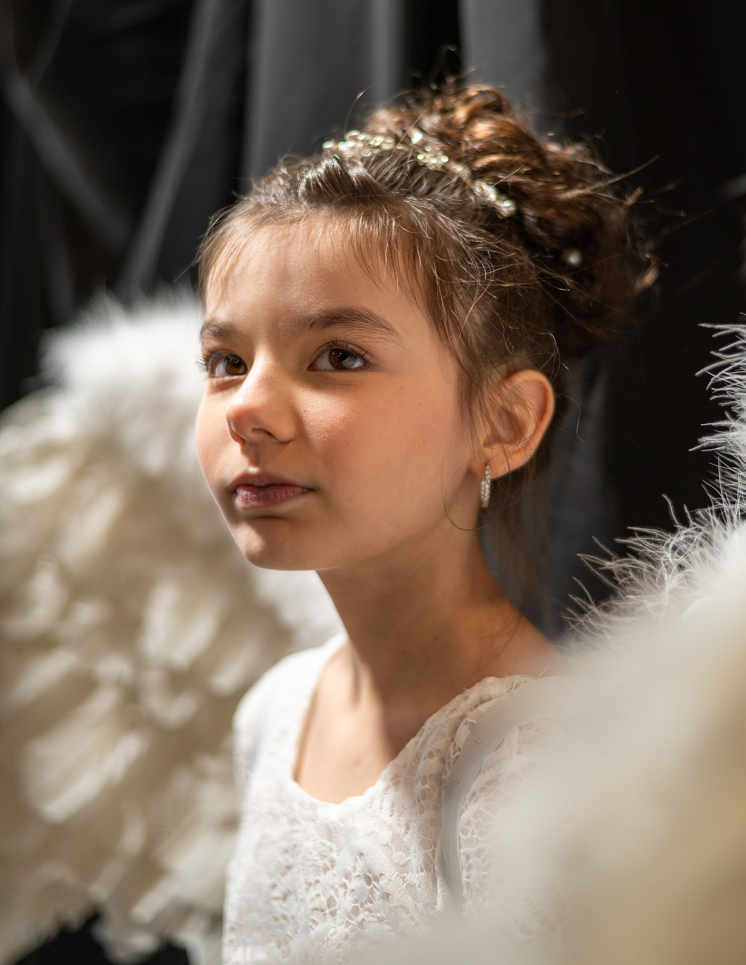Young child wearing white lace dress with hair in updo style and soft lighting in portrait.