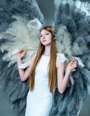 Ethereal fashion portrait with flowing ostrich feathers in blue and white tones against a moody backdrop.