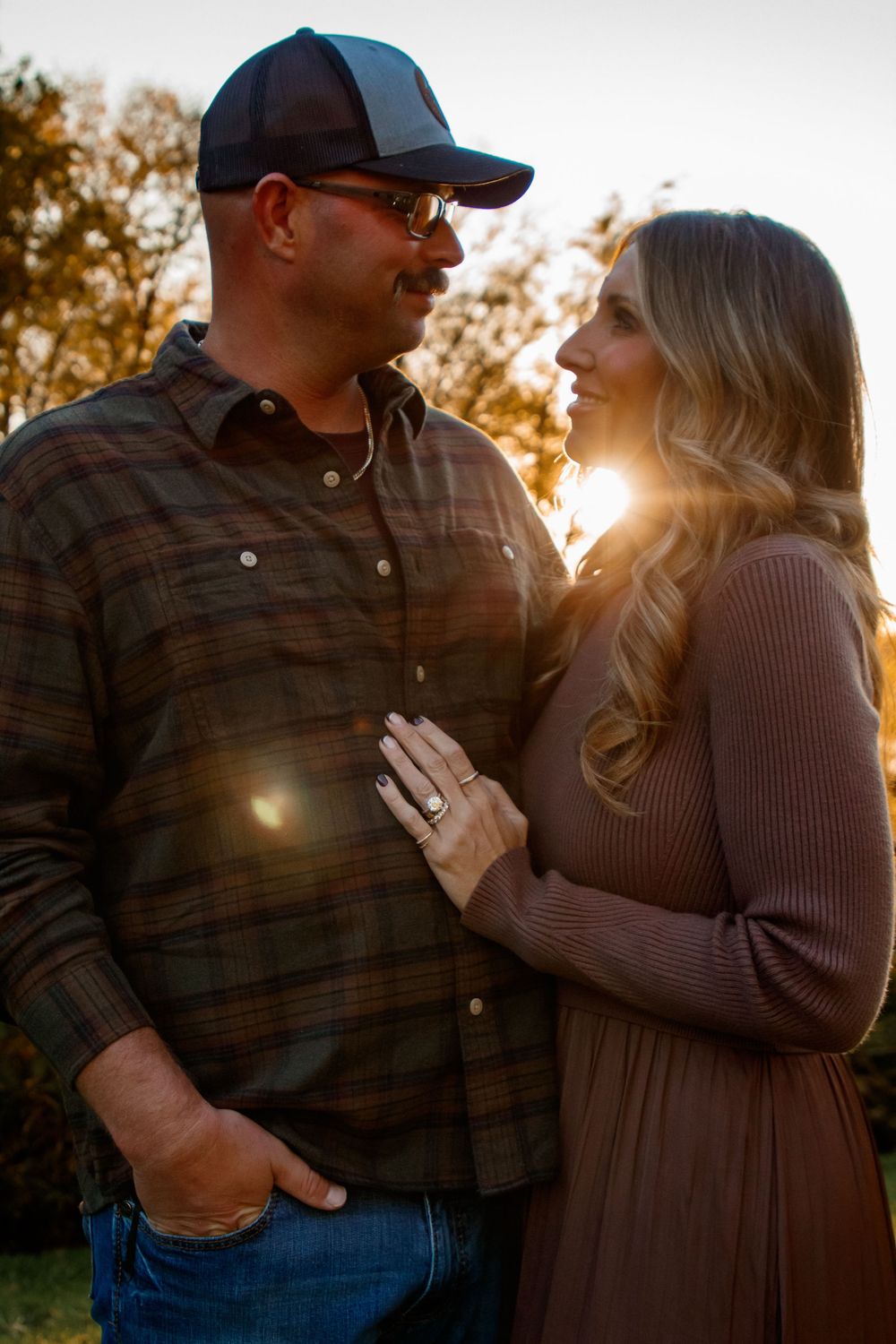 A couple shares an intimate moment at sunset, silhouetted against golden light in a romantic outdoor photoshoot.