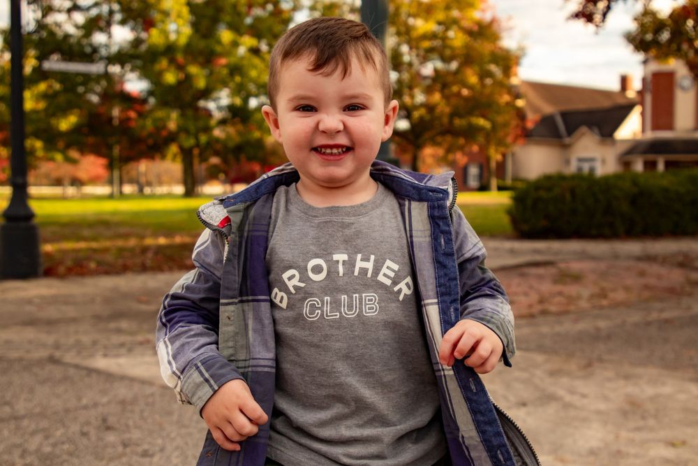 A young child wearing a gray shirt smiles while sitting outdoors during golden hour lighting.
