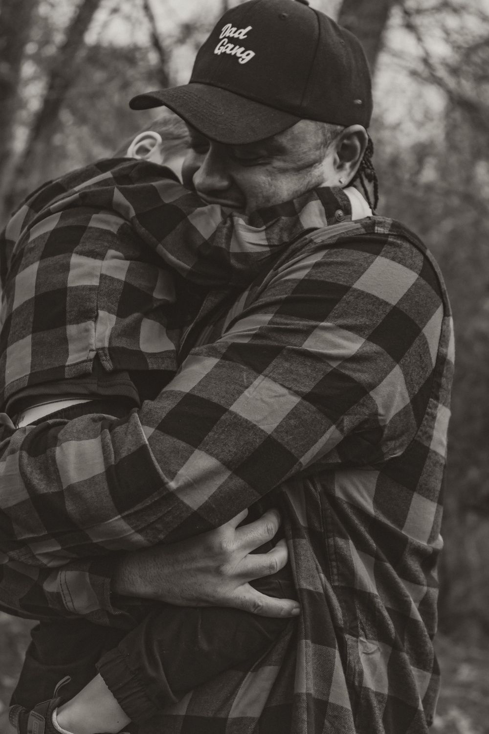 A series of black and white photos showing two people in plaid flannel shirts and baseball caps embracing outdoors.