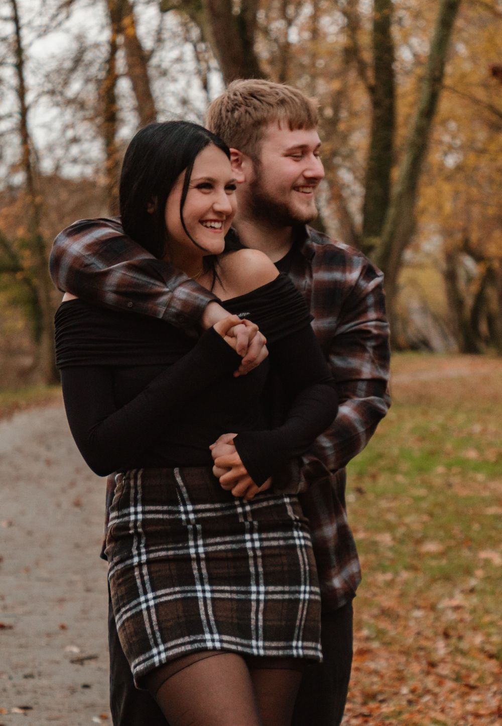 A romantic autumn photoshoot showing a couple in plaid clothing laughing and embracing among fallen leaves.