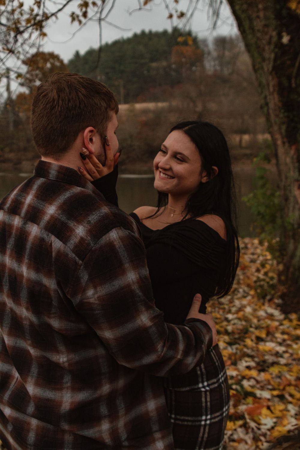 A couple embraces lovingly in a fall setting with autumn leaves scattered on the ground.
